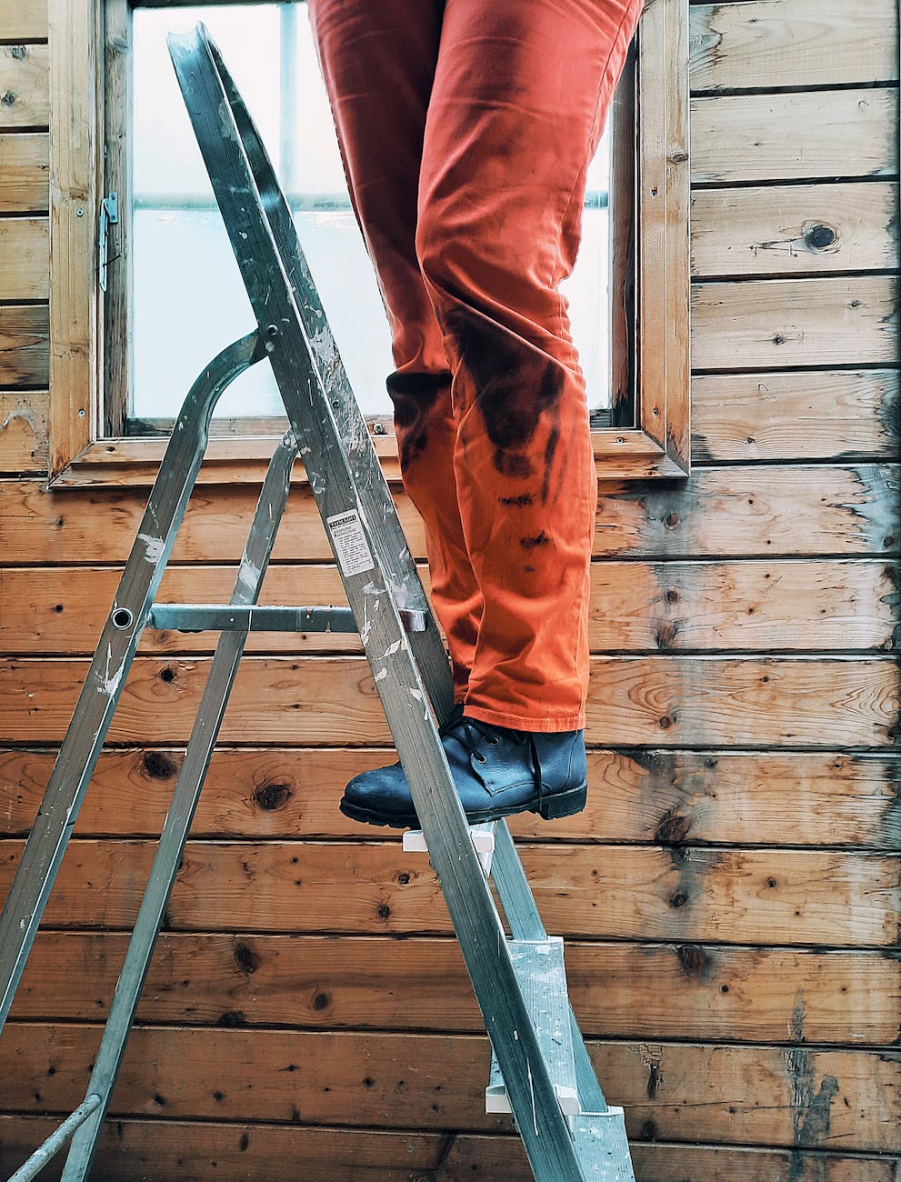 person in orange jeans sitting standing on metal ladder